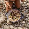 Kind roert met een stok in een pan gevuld met bladeren, stenen en de houten figuren van Grapat